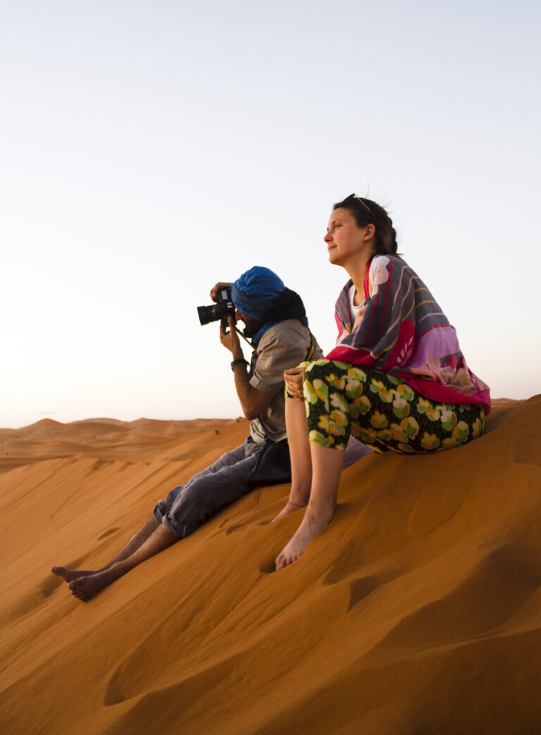 Things to do in Saudi Arabia: two-people-sitting-top-dune-taking-photos