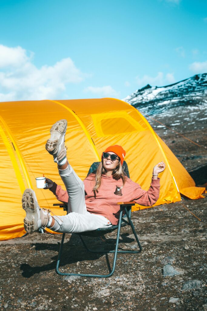funny travel quotes:
Happy female sitting on chair near tent on mountain slope


