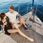 cruises from new york to Canada: Two young attractive europeans sitting on bow of yacht, taling and flirting while on vacation. Lovely couple want to share this today and all their tomorrows. Together they feel carefree.