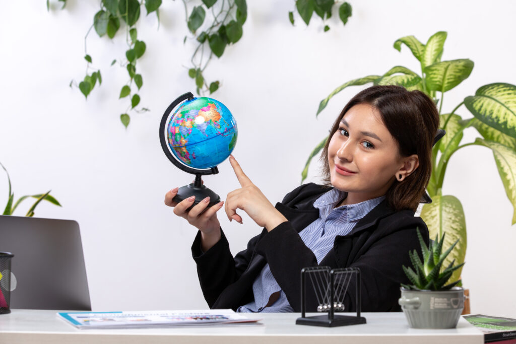 front view beautiful young businesswoman black jacket blue shirt observing little globe smiling front table business job office